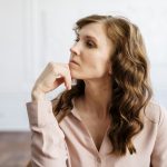 A thoughtful woman with curly hair sits indoors, reflecting deeply in a serene setting.